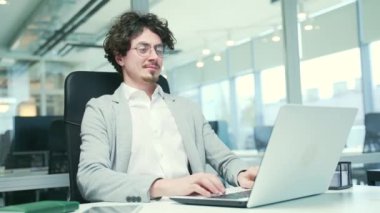 Smiling curly entrepreneur freelancer with hands behind head feels satisfied with work well done Calm bearded businessman relax after hard working day finished project on computer at modern workplace