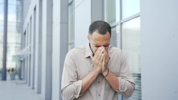 若い大人の男はオフィスビルの外に立っている間 彼は季節のアレルギーを持っているので くしゃみ 男性は風邪やインフルエンザ 気管支炎 呼吸器感染症の最初の症状を持っています — ストック動画