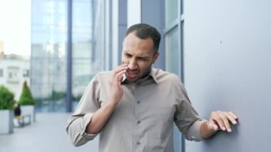 Genç yetişkin bir adam bir ofis binasının yanında dururken diş ağrısı hisseder. Acı çeken üzgün melez erkek yanak yanağa tutuşuyor. Bir dişçinin yardımına ihtiyacı var. Sağlık hizmetleri kavramı