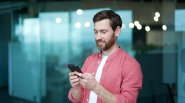 Gülümseyen iş adamı serbest çalışan akıllı telefon ile modern ofis işyerinde sosyal medyayı izleyerek mutlu sakallı girişimci işvereni evde tek başına arama yaparken telefon uygulaması kullanıyor.