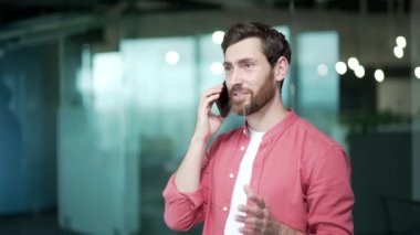 Kendine güvenen iş adamı serbest girişimci modern ofisin içinde cep telefonuyla konuşuyor başarılı, sakallı ofis çalışanı iş yerinde akıllı telefondan profesyonel sohbet yapıyor.