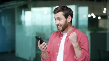 Modern iş yerindeki akıllı telefondan gelen mesajı okuduktan sonra aşırı mutlu iş adamı. Yetişkin girişimci telefon ekranına baktı ve sevindi. Ofiste harika haberler aldı.