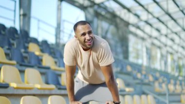 Şehir stadyumunda koştuktan sonra yorgun genç koşucunun nefes darlığı var. Karışık ırktan tükenmiş erkek elleri dizlerinin üzerinde duruyor, derin derin nefes alıyor, terini alnından siliyor.