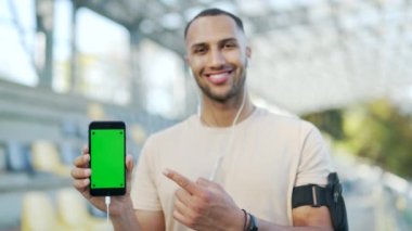 Şehir stadyumunda otururken akıllı telefonu yeşil ekran ile gösteren genç sporcuyu kapat. Karışık ırk erkek, cep telefonu rengini işaret ediyor. Reklam için dikey model şablonu.