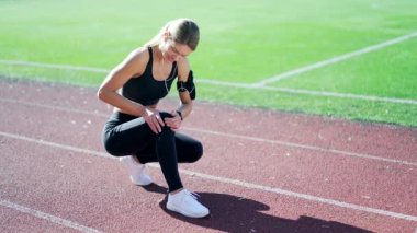 Yetişkin bir bayan sporcu, şehir stadyumunda diz ağrısı ve spor sakatlığından muzdarip. Spor kıyafetleri içinde üzgün bir kadın, masaj yapıyor ve bacağını ovuyor. Yazın sokakta antrenman yaptıktan sonra sorun çıkarıyor.