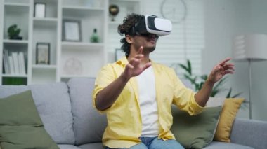 Adam evdeki koltukta otururken sanal gerçeklik kulaklığı kullanıyor. Modern sanal eşyalara dokunan mutlu genç erkek ya da kapalı mekandaki düğmeye basıyor.