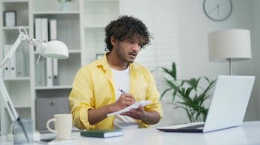 Genç serbest çalışan iş adamı ya da öğrenci internetten video yoluyla ders çalışıyor. Not defterine not alıyor. Giyim ya da uzak kurs ev ofisteki dizüstü bilgisayarı kullanarak bir toplantı veya konferans eğitimi