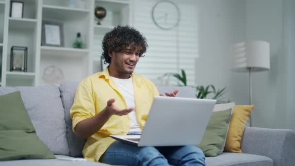 快乐快乐的人通过笔记本电脑通过视频电话与家人或朋友在线交流 一个穿着黄色衬衫的男人坐在沙发上遥谈 挥挥挥手 微笑着 — 图库视频影像
