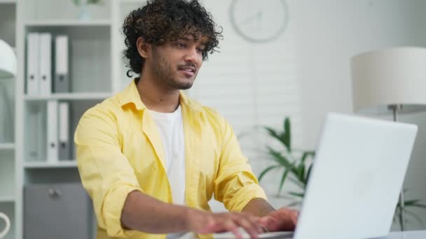 若いインドの男性従業員の起業家やフリーランスは オフィスや自宅で職場でラップトップコンピュータを使用してオンラインでタイピングブラウジング作業プログラマの労働者エージェントやコーダーは 忙しい仕事のメモ帳を持っています — ストック動画