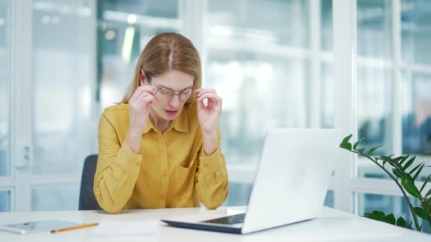 疲れ切った金髪熟女は職場でのコンピューターの働き過ぎ後に痛みの痛みで目をマッサージするために眼鏡をはずし悪い視力を傷つけます視覚疲労と眼精の概念 — ストック動画