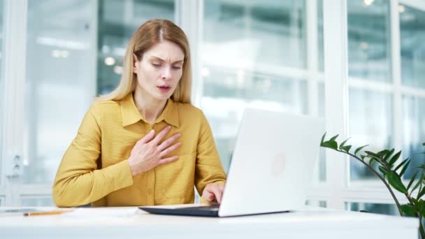 心配している成熟したビジネス女性の肖像は 現代の職場でラップトップを入力しながら パニック心臓発作で胸に手を取りますオフィスで精神衛生上の問題を持つ不安ブロンド女性起業家 — ストック動画
