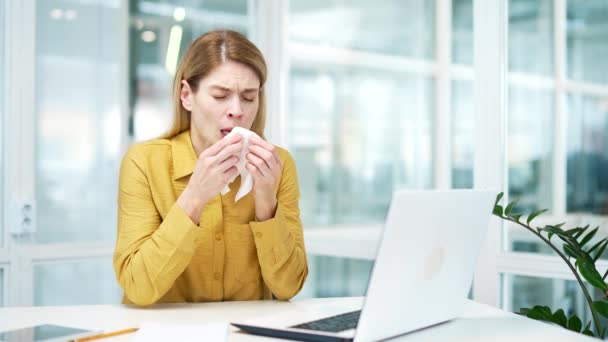 アレルギー不健康な成熟したビジネス女性起業家くしゃみで組織を吹いて鼻アレルギーウイルス風邪熱の症状は 現代のガラスの職場で机の上にコンピュータの横に座っている — ストック動画