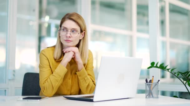 職場でノートパソコンを入力しながら 現在のプロジェクト解決の問題の成功戦略を考え眼鏡を持つ思慮深いブロンドの成熟したビジネス女性起業家の肖像 — ストック動画
