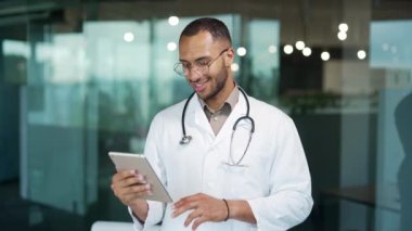 Klinikte dururken tablet kullanan gülümseyen genç bir doktorun portresi. Gözlüklü ve beyaz önlüklü yakışıklı bir ırk terapisti internetten haberlere bakıyor, mesajlara cevap yazıyor, e-posta okuyor.