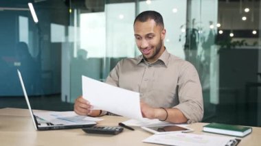 Genç yetişkin işadamı, görevdeyken elinde tuttuğu mali rapordan memnun. Karma ırk finansörü sonuçlardan memnun ve evet jestiyle kutluyor.