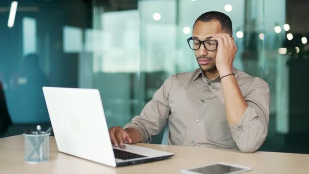 남자는 직장에서 사무실의 책상에 노트북을 사용하는 노동자는 안경을 손으로 다리를 — 비디오