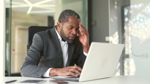 現代のオフィスの机に座っている間 ラップトップで悪いニュースを受け取る正式な訴訟で不安成熟したアフリカ系アメリカ人男性 悲しい中年のビジネスマンは ビジネスの損失について不快なメッセージを読み取ります — ストック動画