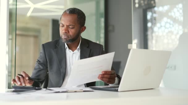 在现代办公室工作时 专心致志的非洲裔美国金融家手里拿着正式的戴着文件 在计算器上查看数据 会计师分析财务报告 — 图库视频影像