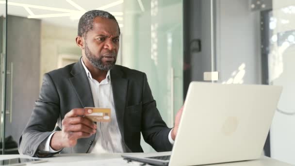 Расстроенный Африканский Американец Держит Кредитку Смотрит Экран Ноутбука Сидя Офисе — стоковое видео