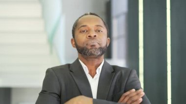 Ciddi bir Afro-Amerikan iş adamının kapalı bir ofis binasında kameraya bakarken çekilmiş portresini yakından çek. Resmi takım elbiseli çapraz kollu, kendinden emin orta yaşlı bir sahibi var.
