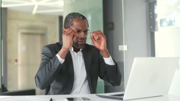过度劳累的 成熟的 身穿正式西装的非洲裔美国人 坐在办公室工作时 觉得在笔记本电脑上工作太累了 一位中年男子摘下眼镜 按摩鼻梁 — 图库视频影像