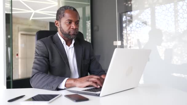 オフィスに座っている間 ラップトップで働く正式な訴訟で成熟したアフリカ系アメリカ人男性を確信しています 中央集権的な中年実業家はインターネット上でビジネス情報を閲覧し — ストック動画