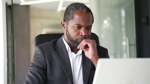 在办公室里 一个穿着正式西服 头脑清醒的成熟的非洲裔美国男人坐在一个使用笔记本电脑的工作场所 全神贯注的中年商人正在考虑一桩严肃的生意 — 图库视频影像