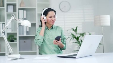 Kıvırcık esmer genç bir kadın akıllı telefon uygulaması kullanıyor. Modern ofiste müzik sesi ya da kulaklıkla radyo dinleyen bir çalışan. Kapalı alandaki iş yerinde çalışan hoş bir kız öğrenci telefon listesinden keyif alıyor.