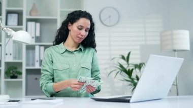 Mutlu kadın işçi işyerinde otururken nakit dolarları sayar. Serbest çalışan kadın girişimci, iş kadınlarının kazançlarını hesaplıyor. Nakit para, para, maaş, maaş...