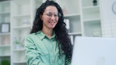 Modern hafif iş yerinde dizüstü bilgisayarda çalışan Latin kökenli genç işkadını. Gözlüklü, meşgul girişimci, harika iş gününün tadını çıkarıyor ve ofiste yazı yazarak arama yapıyor. Kapatın.