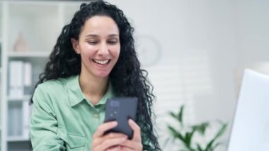 Yakından bakınca, sevimli İspanyol Arap iş kadını akıllı telefon daktilo kullanıyor kayan kaykay kayıyor, cep telefonu kullanıyor iş yerinde kapalı ofis içinde mutlu kıvırcık esmer işçi uygulamasını kullanıyor.