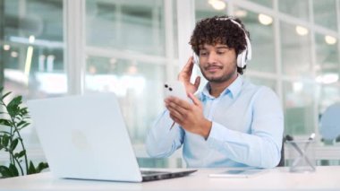 Modern ofisteki çalışma masasında otururken kulaklık takmış, akıllı telefondan müzik dinleyen genç bir işçi. Yakışıklı bir adam işe ara verip en sevdiği şarkıyı dinler.