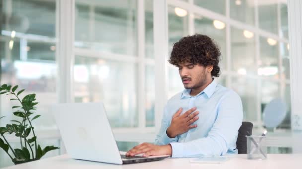 現代オフィスのデスクで仕事をしながらノートパソコンで働く中 胸焼けに苦しむ病弱の青年 悲しい労働者は消化不良 急性胃炎や胃潰瘍を持っています — ストック動画
