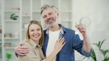 Yeni dairenin mutlu evli çiftleri kameraya bakarak yeni evin anahtarını gösteriyor. Olgun eş ve koca kucaklaşır ve gülümser, yeni evde sevinir, oturma odasında dururlar.