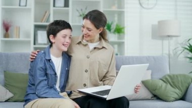 Genç anne evdeki kanepede otururken internetten oğluyla bir video görüşmesi yapıyor. Çocuklu mutlu bir kadın, ailesiyle uzaktan konuşan bir çocuk.