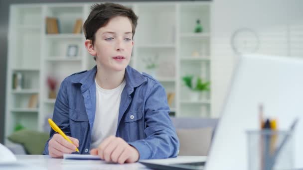 ある少年はビデオ通話で遠隔講義を学ぶ 遠隔学習は コースやウェビナーを聞き ノートブックに注意してくださいE教育家庭でノートパソコンを使用して遠隔教師の学校の少年 — ストック動画