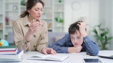 Yorgun bir anne okul çocuğu ile ödev yapıyor. Oğlunu azarlarken aynı zamanda ders çalışmasına yardım ediyor. Evde yorgun, tembel okul çocuğu. Ebeveynler sıkılmış çocuklara öğretiyor.