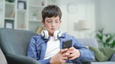 Okullu bir çocuk evdeki kanepede otururken akıllı telefon kullanıyor. Kapalı alanda. Kulaklık takan, daktiloyla konuşan, cep telefonu kullanan modern bir çocuk. Bağımlı okul çocuğu konsepti