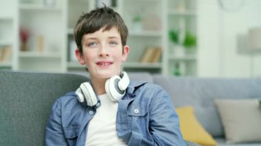 Yüzünde çilleri ve kulaklıkları olan, evde, odasındaki bir kanepede mutlu bir şekilde oturan mavi gözlü bir okul çocuğunun portresi. Vesikalık, modaya uygun, modern genç kız.