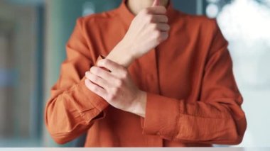 Modern bir ofisin çalışma masasında otururken bileğine masaj yapan bir kadının elini kapat. Kadın bir çalışan eklem ağrısından muzdarip, yaralanmış, ağrıyan bir kası ovuyor, egzersiz yapıyor.