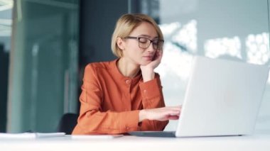 Modern ofisteki çalışma masasında otururken iş yerinde dizüstü bilgisayarla çalışmaktan sıkılan üzgün genç bayan çalışanlar. Yorgun, sarışın kadın işe konsantre olamıyor, dikkati dağılıyor, dinlenmek istiyor.