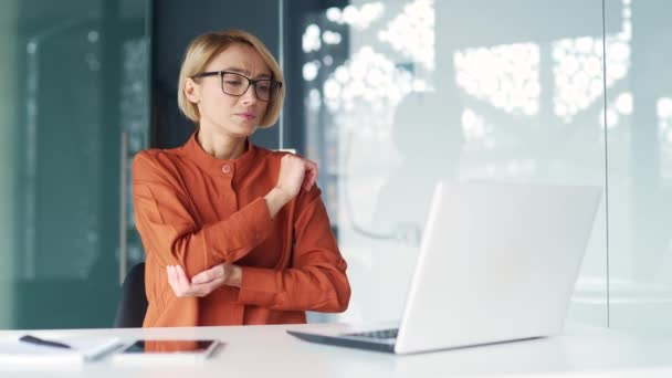 在现代办公室的办公桌前工作时 疲惫不堪的年轻女性在笔记本电脑上工作时手肘酸痛 戴眼镜的一位悲伤的女员工正在按摩关节 伸出手来 — 图库视频影像