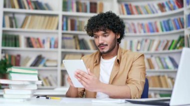 Üniversite öğrencisi kampüs kütüphanesinde tablet kullanıyor. İnternette bilgi arayan mutlu üniversite öğretmeni ya da bir arkadaşla sohbet eden, kısa mesaj yazan, e-posta ya da sosyal medyayı kontrol eden