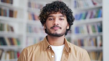 Gülümseyen ve kameraya bakan genç bir üniversite öğrencisinin portresini yakından çek. Kampüs kütüphanesinde poz veren mutlu, dost canlısı üniversite öğretmeni. Zeki bir erkek bir sınıfta duruyor.