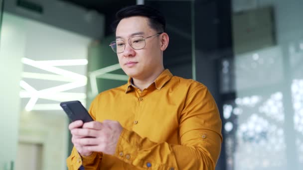 Poważny Azjatycki Biznesmen Okularach Używa Przeglądając Smartfona Stojąc Nowoczesnym Biurze — Wideo stockowe
