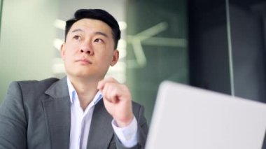 Ofiste dizüstü bilgisayarın başında otururken sorun çözmeyi düşünen düşünceli Asyalı işadamlarına yakın çekim. Resmi takım elbiseli ciddi bir komisyoncu borsadaki online verileri analiz ediyor.