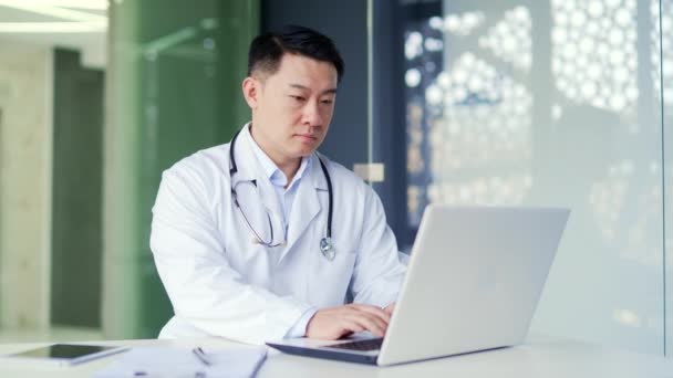 Beyaz Önlüklü Ciddi Bir Asyalı Doktor Modern Hastane Kliniğindeki Işyerinde — Stok video