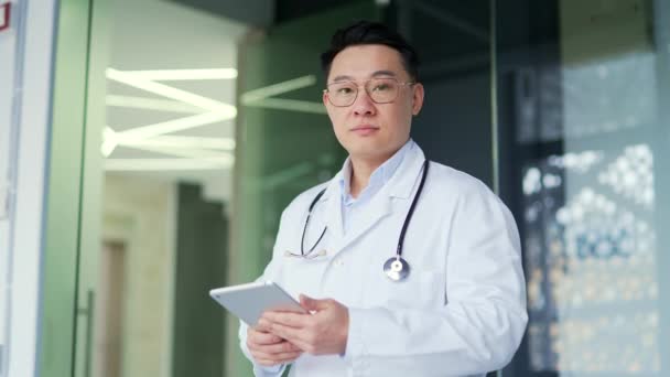 Portret Poważnego Azjatyckiego Lekarza Białym Płaszczu Trzymającego Tabletkę Stojącego Nowoczesnej — Wideo stockowe