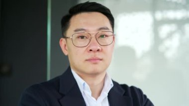 Modern bir ofiste duran resmi takım elbiseli ve gözlüklü ciddi bir Asyalı işadamının portresi. Kendine güveni olan, patron, kameraya bakıp poz veren yatırımcı. Girişimcinin kafasından.