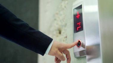 Mans asansör aşağı tuşuna elle basıyor. Erkek parmağının gümüş metal düğmeye basarak asansöre binmesine yaklaş. Takım elbiseli bir işadamı asansörün ofis binasına gelmesini bekliyor.